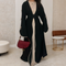 Woman wearing a black and beige dress with a red handbag in an indoor setting.
